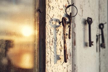 Old rusty key on the wooden door frame with broken white paint with a blurred reflection of a sunset on a dirty glass