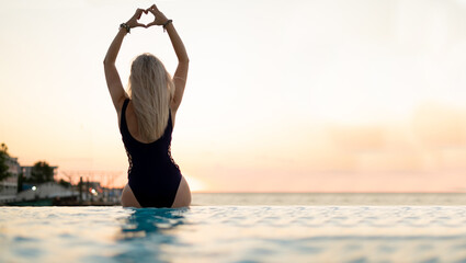 Woman by the pool. Hands up enjoying the view from the endless rooftop pool in Asia. She raised her...