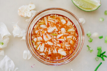 Vietnamese Fish Sauce (Nuoc Cham)  made with fish sauce, garlic, lime, and red chilis. Horizontal photo of Viet dipping sauce, surrounded by a lime wedge and garlic leftovers.  