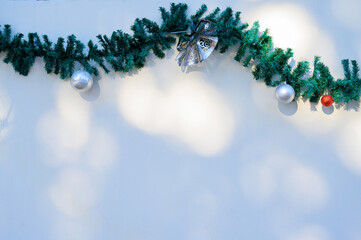 Christmas decoration. Garland with green spruce branches ana a white wall.