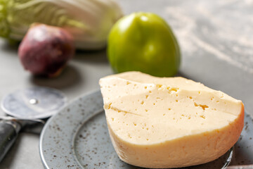 A piece of cheese on a plate next to vegetables and a pizza knife