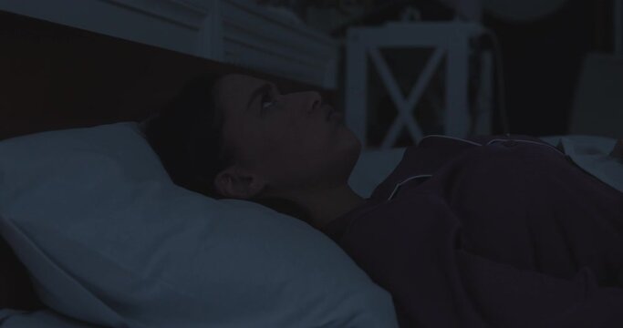 Young irritated woman covering ears with pillow in bed late at night