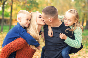 Fototapeta premium Portrait of young family playing in autumn park. Parents kissing and resting with children in the autumn park