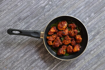 Chicken fry or Fried chicken kabab which is well garnished with curry leaves in a black frying pan with grey background 
