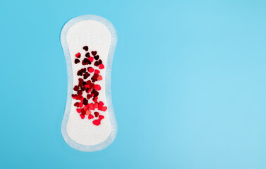 Daily, one-time white feminine pad with red hearts as a symbol of blood secretion. Woman health concept, menstrual cycle, ICP, period. Blue flat lay background with copy space.