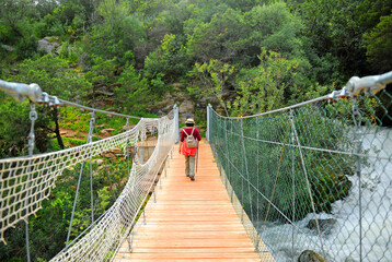Obraz premium Woman with backpack crossing a wooden footbridge in the Guadiaro river near the Canyon of the Buitreras famous gorge located in the Alcornocales Natural Park Malaga province Andalusia Spain