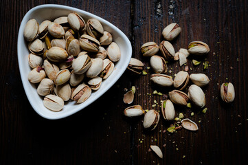 Pistachio nuts in a white bowl top down on wood.