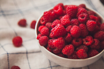 Pile of fresh raspberry in a white plate top view of red berries on the white napkin. Summer feeding concept. Summer berries concept. 