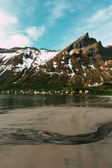 Beautiful day on the norwegian beach. Stream flowing into the sea. Amazing mountains and colorful scandinavian village in the background. Fjord on the northern Norway, Senja island.