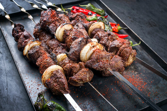 Traditional Russian shashlik on a barbecue skewer with chili, onion and sumach as close-up on a rustic metal tray