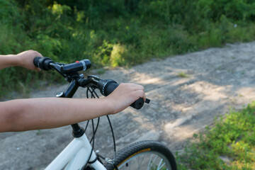 boy's hand holds black handlebar of bike while he is riding bicycle on countryside road in green forest. Happy summer vacation concept.