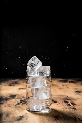 Gin and tonic cocktail recipe, ice cubes falling, highball glass, wooden table, dark background