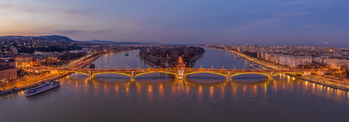 Panoramic Aerial drone shot of Margaret Bridge with lights on over Danube river during Budapest sunset