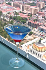 coctel martini de curacao azul con cereza, de fondo vista panorámica de la ciudad