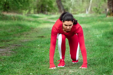 A girl in a tracksuit is preparing to run, physical exercises against the backdrop of nature, prelaunch pose. The concept of a healthy lifestyle, exercise, fresh air. Copy space.