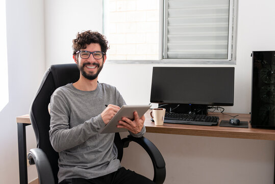 Hispanic man in his office working with tablet looking at camera smiling. Home office concept.