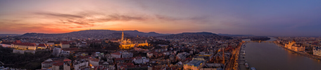 Panoramic aerial drone shot of lighted Matthias Churh Buda castle on Buda Hill by Danube in Budapest sunset