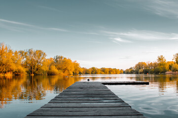 Idyllic peaceful lake with a wodden pier and colorful orange autumn tones with sunset light. Germany