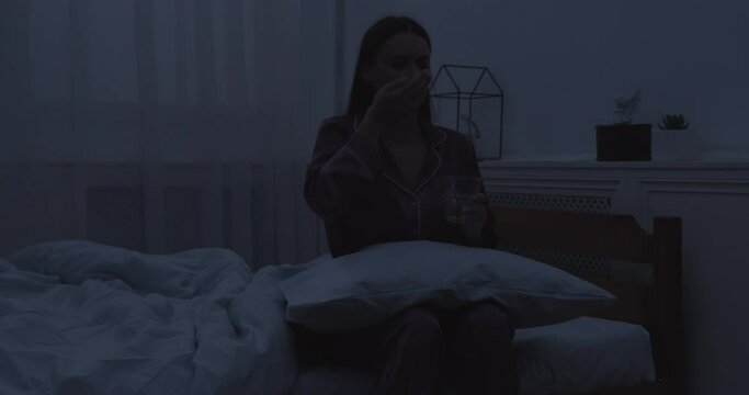 Young woman sitting on bed, taking sleeping pills in bedroom