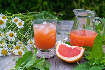Grapefruit juice with ice cubes ,mint leaves and a bunch of daisies in the open air on a green blurred background.