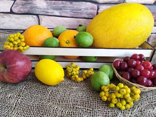 Fruit and berry still life yellow oval melon orange lemon red apple green unripe walnuts and yellow rowan in a wooden box on the kitchen table