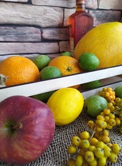 Fruit and berry still life yellow oval melon orange lemon red apple green unripe walnuts and yellow rowan in a wooden box on the kitchen table