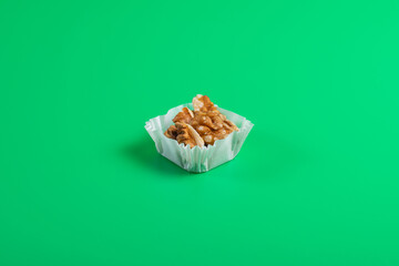 portion of walnuts in a paper muffin cup on a green background