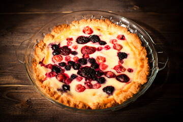 Baked round homemade cheesecake with berries. Pie on an old dark wood table. Flatlay background.