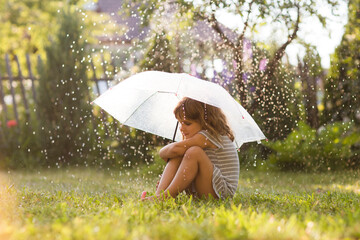 child girl with umbrella in summer rain in the garden
