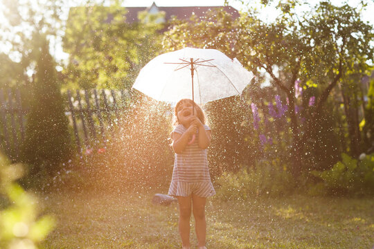 Child Girl With Umbrella In Summer Rain In The Garden