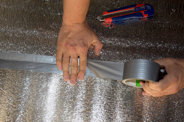 A man hides a foil isol with reinforced tape. Male hand holds reinforced tape. Repair in the apartment, floor insulation.
