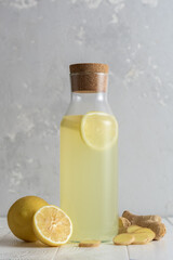 Decanter with ginger water and lemon on white table.