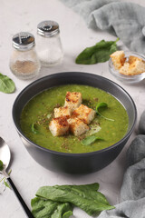 Green spinach puree soup served with croutonsin a dark bowl on a gray concrete background, Closeup