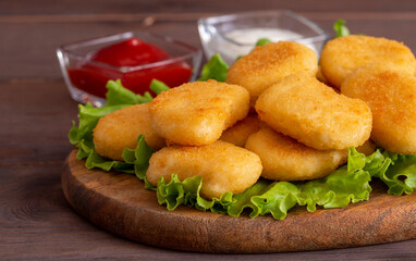 Delicious crispy fried chicken nuggets with sauce close-up on the board. Side view. A bunch of nuggets.