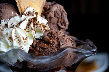 Close Up Still Life of Scoops of Chocolate Ice Cream topping with wipe cream cream and waffle cracker in glass bowl in black background, Macro with shallow dof, Cold refreshing summer dessert