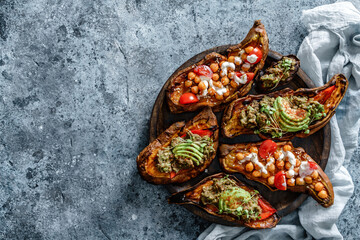 Baked sweet potato toast with roasted chickpeas, tomatoes, goat cheese, sauce guacamole, avocado, seedlings on wooden board over blue background. Healthy vegan food, clean eating, dieting, top view