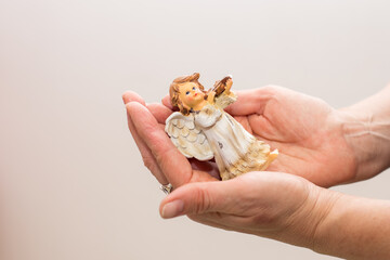 statuette in the form of an angel in women's hands on a light background