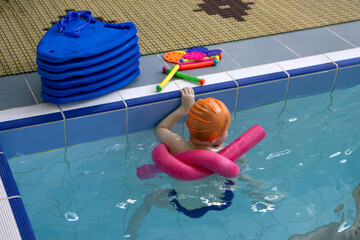 Cute little toddler boy child kicking feet in swimming costume use pool noodle and kickboard learn to swim at indoor pool, Swimming school for children concept