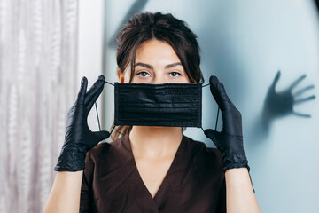 portrait of young female beautician in black medical mask looking at camera