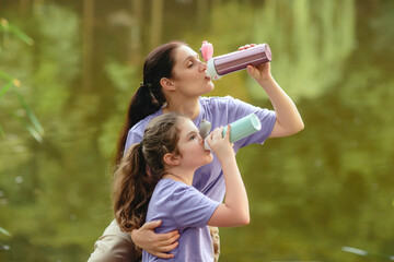 Close-up of mother and daughter on a walk in the park drinking from vacuum flask. Concept of outdoor recreation using reusable dishes. A bottle for coffee or tea to go.