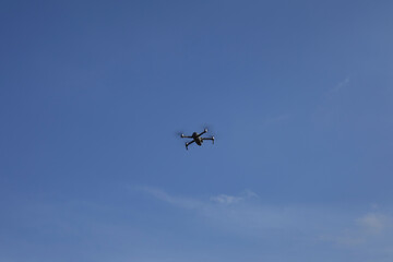 Quadrocopter drone flying in far in the blue sky