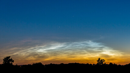 NLC clouds. Noctilucent clouds above rural field 