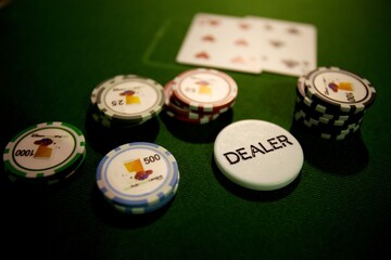 Chips and playing cards at a casino card game with dealer chip on green baize
