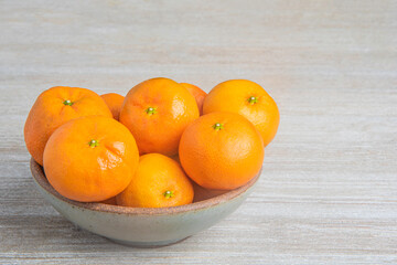 Fresh Oranges In A Ceramic Bowl Set On Wood Panel