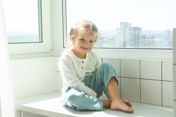 Little cute girl in a bright room, a minimum of objects in the room, the child rejoices, sitting by...