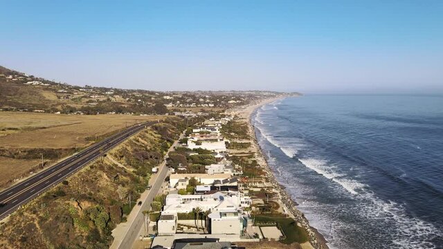 Drone shot moving over houses along pacific ocean in Malibu on a beautiful summer day