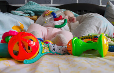 Small legs next to many toys on a light background. Legs in socks and pants. Rattles at the feet of the child. Close-up.