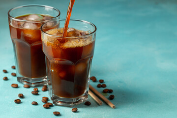 Ice coffee in a tall glass with cream poured over and coffee beans on a light stone background. Cold summer drink with tubes. With copy space