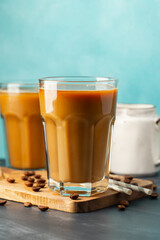 Ice coffee in a tall glass with cream poured over and coffee beans on a light stone background. Cold summer drink with tubes