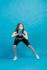 Fototapeta na wymiar Fitness girl wearing medicine mask in fitness costume isolated on blue background. Training during quarantine, covid 19, coronavirus.